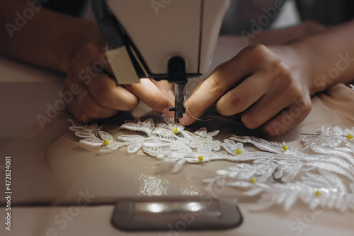 Somebody is sewing an ornament on the table with the help of machine.