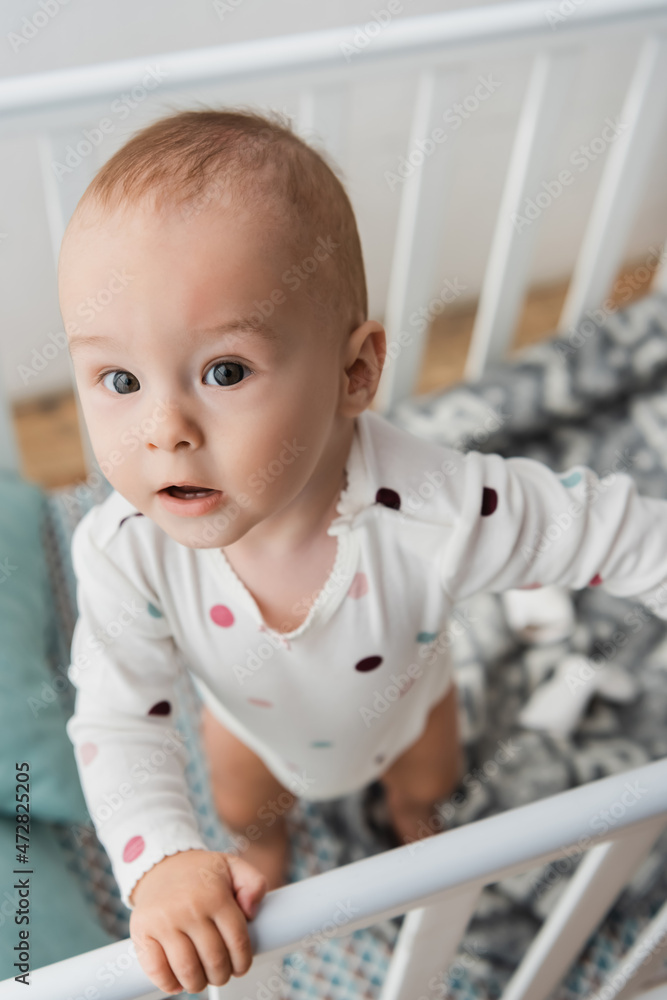 high angle view of little boy standing in crib at home. high angle view of little boy standing in crib at home.