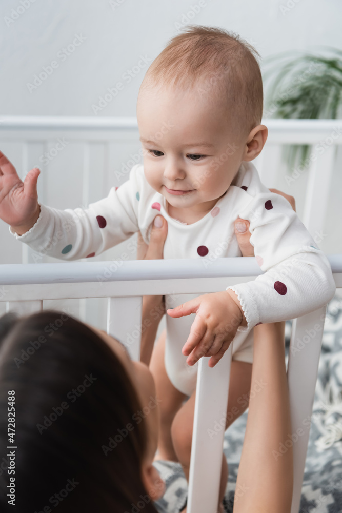 blurred woman holding smiling little son in crib. blurred woman holding smiling little son in crib.