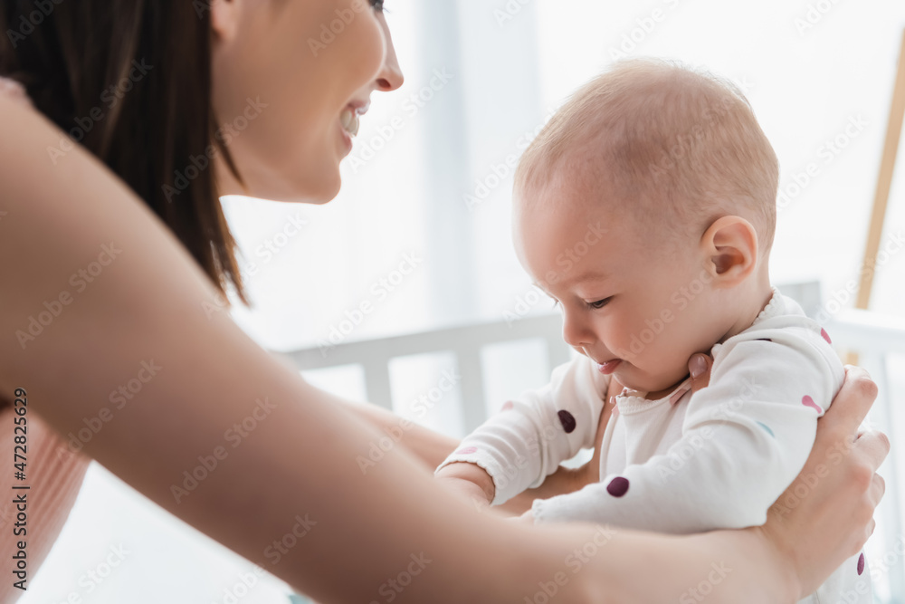 blurred woman smiling while holding baby boy in crib. blurred woman smiling while holding baby boy in crib.