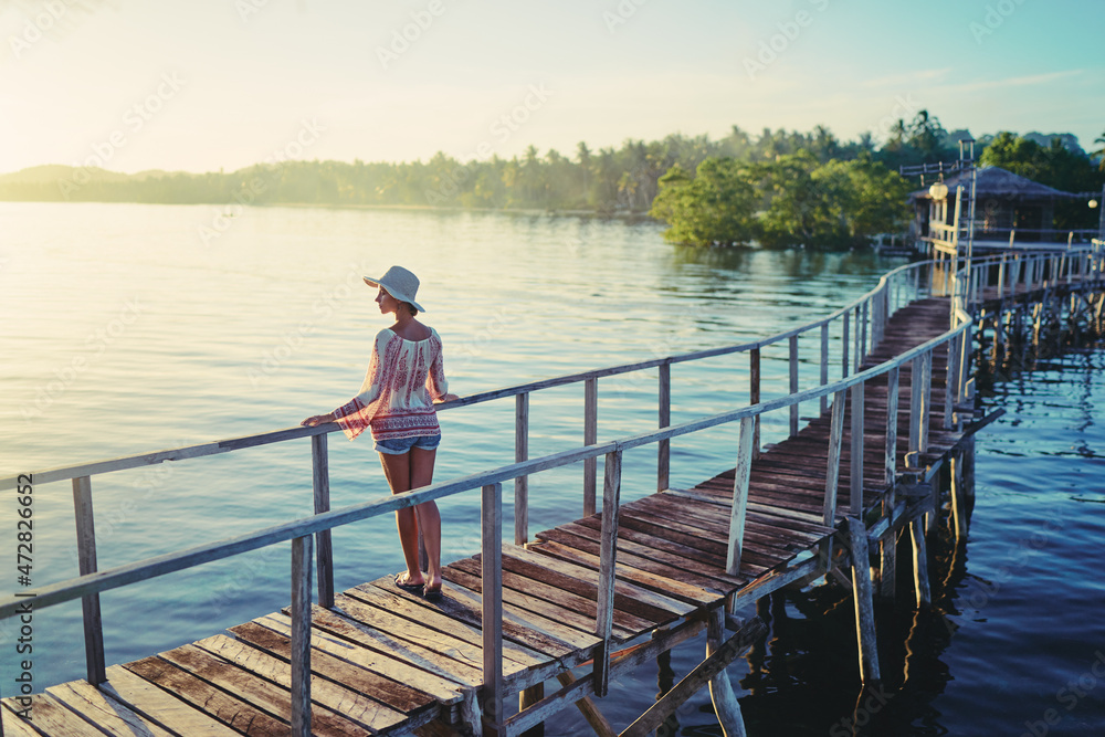Vacation on tropical island.  Back view of young woman in hat enjoying sunset sea view from wooden bridge terrace, Siargao Philippines