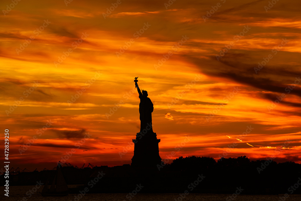 Naklejka premium Travel to Manhattan, visit New York. Amazing summer sunset over Statue of Liberty with spectacular dramatic sky. One of the most known landmark in United States.