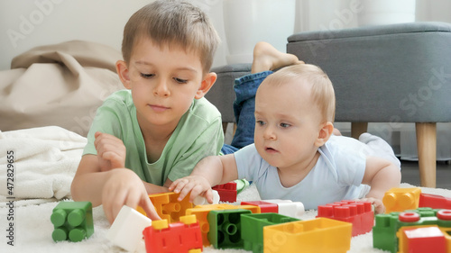 Little baby boy with older brother playing toy blocks and bricks on carpet in living room. Concept of children development, education and creativity at home