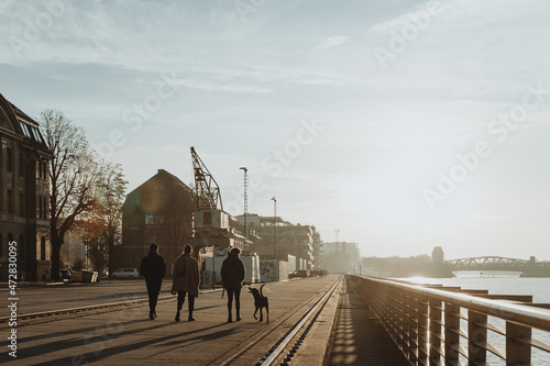 Photography People walking with a dog along the waterfront at sunset in an urban harbor area