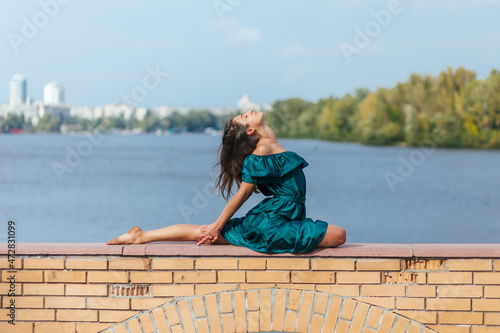 beautiful girl in green dress doing yoga poses in the autumn park near the river, balance, fitness, stretching and relaxation