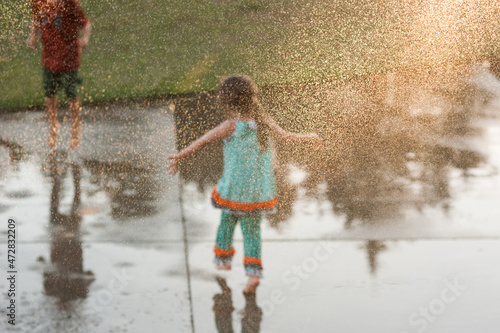 A Kid Child Young Girl Boy Plating in the Rain Water Sprinkler Fun Childhood Unplugged Get Outside Sun Grass Concrete Sunshine 
