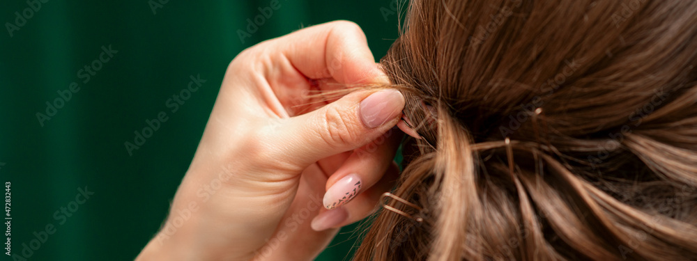 Fototapeta premium Hairdresser makes hairstyles for a young woman in beauty salon close up