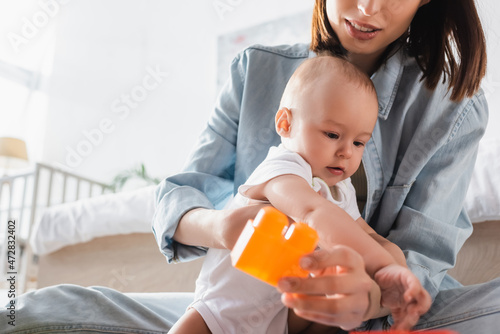 woman holding toy building block while playing with son at home.