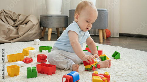 Cute baby boy sitting on carpet and playing with colroful plastic toy car. Concept of children development, education and creativity at home