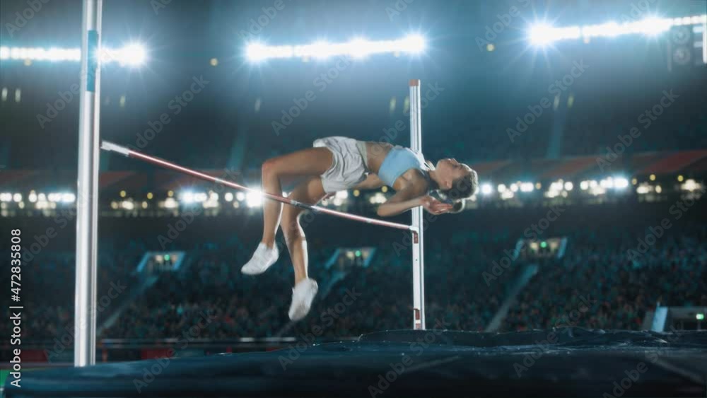 High Jump Championship: Professional Female Athlete Running, Successfully Jumping over Bar. Sportswoman Celebrates Winning with Stadium Full of Spectators Cheering. Cinematic Static Shot, Slow Motion