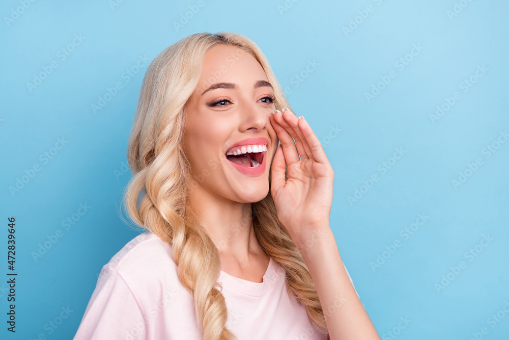 Photo of cute young blond lady talk secret wear pink t-shirt isolated on blue color background Photo of cute young blond lady talk secret wear pink t-shirt isolated on blue color background