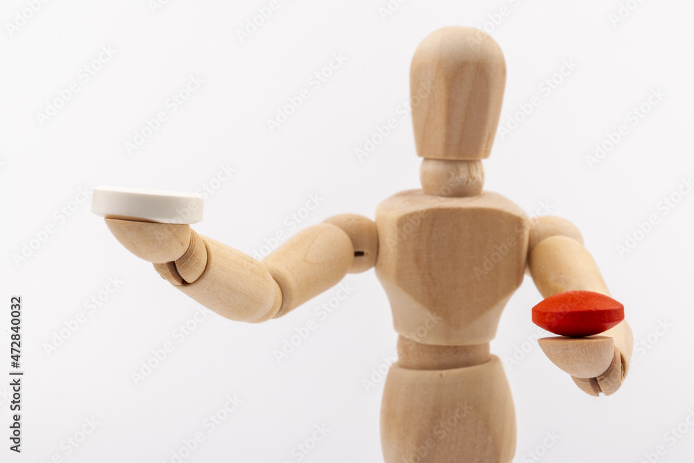 A wooden Gestalta doll or mannequin holds red and white pills in its hands on light background. The concept of choice. A wooden Gestalta doll or mannequin holds red and white pills in its hands on light background. The concept of choice.
