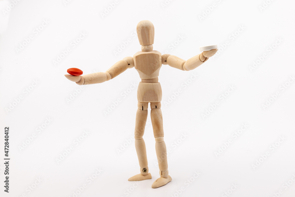 A wooden Gestalta doll or mannequin holds red and white pills in its hands on light background. The concept of choice. A wooden Gestalta doll or mannequin holds red and white pills in its hands on light background. The concept of choice.