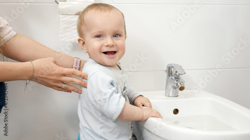 Portrait of cute baby boy standing at toilet and splashing water. Concept of child development, fun and education at home.