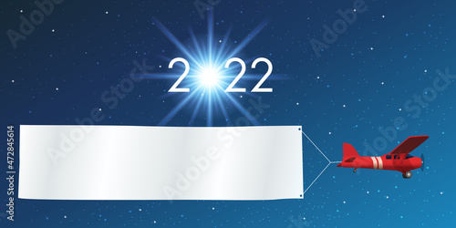 Carte de vœux 2022 montrant un avion rouge tirant une banderole blanche pour souhaiter la bonne année, devant un ciel étoilé. photo