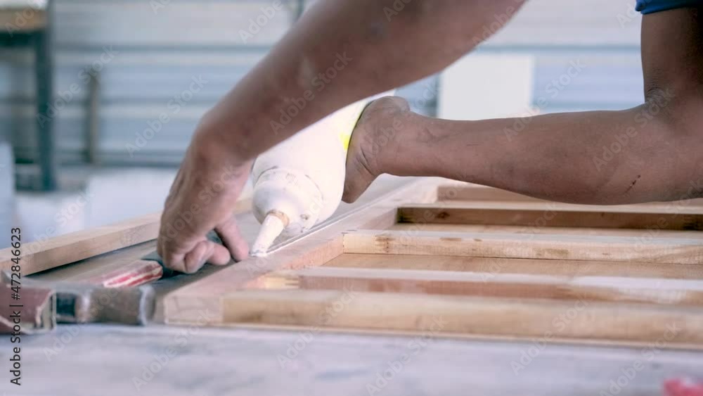 carpenter's hand who is assembling the built-in cabinet, pressing white latex onto the wooden frame with the unique technique of a carpenter with free hand in the warehouse carpenter's hand who is assembling the built-in cabinet, pressing white latex onto the wooden frame with the unique technique of a carpenter with free hand in the warehouse
