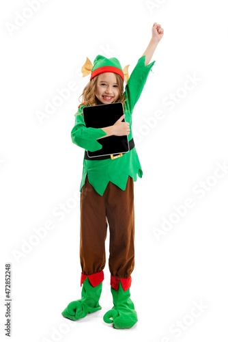 Cute smiling girl dressed like funny gnome or elf using tablet, gadget isolated over white studio background. Winter, holiday, christmas concept