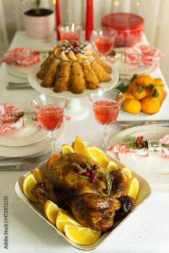 Beautifully decorated festive table with baked chicken, homemade cake, glasses of wine and candles. Baked chicken for Thanksgiving, Christmas and New Year.