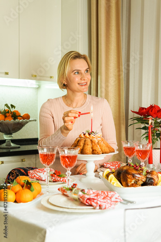 A lovely 40-year-old woman is sitting at a festive table, smiling and holding a candle in her hand. Christmas Holiday, Thanksgiving Day, New Year.
