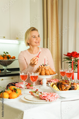 A lovely 40-year-old woman is sitting at a festive table, smiling and holding a candle in her hand. Christmas Holiday, Thanksgiving Day, New Year.