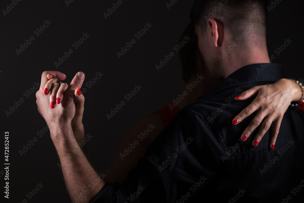 A man in black and a woman dancing tango in the dark; two hands are entwined, she hugs him by the shoulders. - obrazy, fototapety, plakaty 