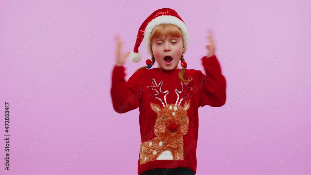 Oh my God Wow. Toddler girl in Christmas sweater raising hands in surprise looking at camera with big eyes shocked by sudden victory isolated on violet background studio. Happy New Year holiday eve Oh my God Wow. Toddler girl in Christmas sweater raising hands in surprise looking at camera with big eyes shocked by sudden victory isolated on violet background studio. Happy New Year holiday eve