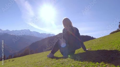 after resting on the top of the mountain after hiking, a female traveler sits down on the grass and admires nature, the view from behind, exploring natural attractions. georgia, svaneti kheshkili. photo