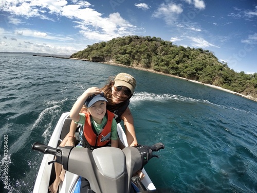 Billede på lærred Mother and son on a jet ski in the ocean with an island in the background