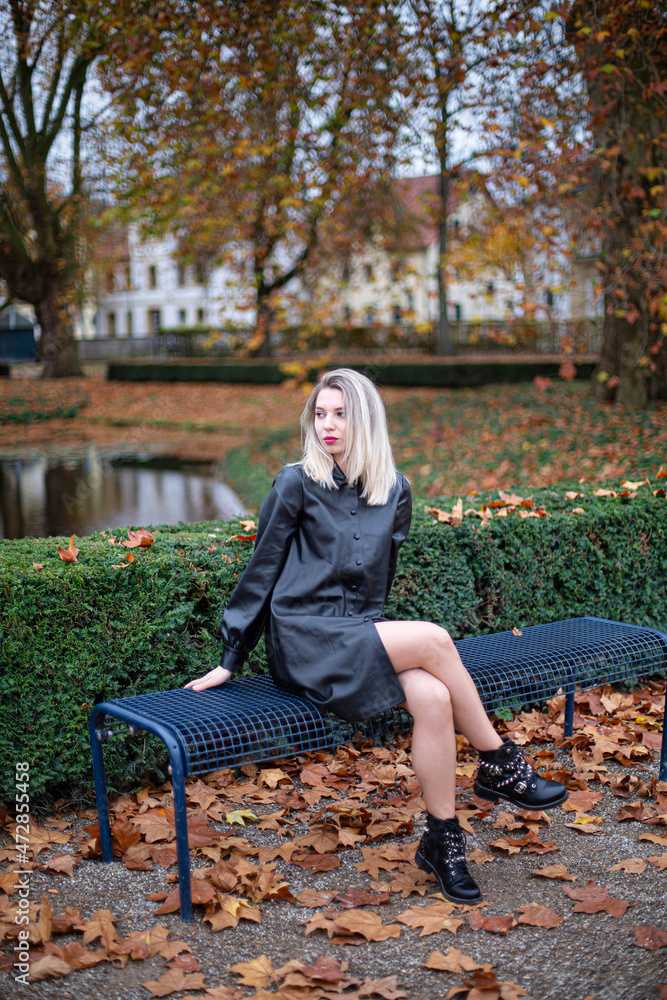 White young european woman with blonde hair in total black sitting on bench in autumn park White young european woman with blonde hair in total black sitting on bench in autumn park
