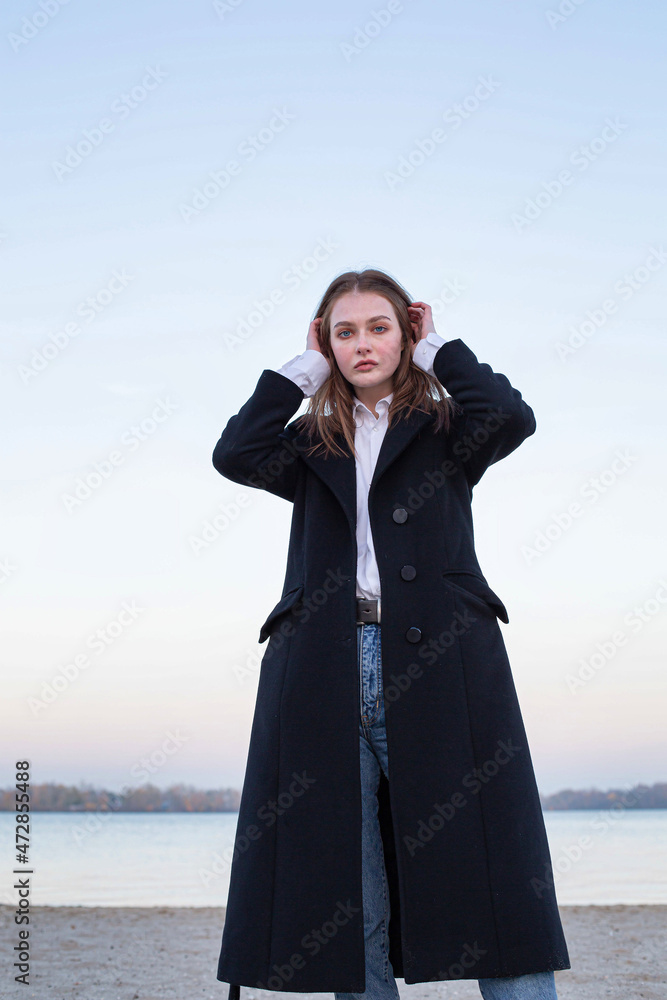 Pretty long straight haired white european woman in dark coat in autumn on the beach Pretty long straight haired white european woman in dark coat in autumn on the beach