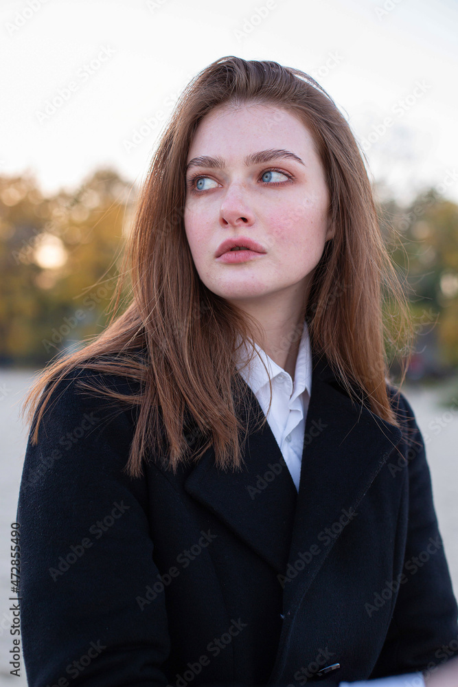 Portrait of pretty long straight haired white european woman in dark coat in autumn on the beach