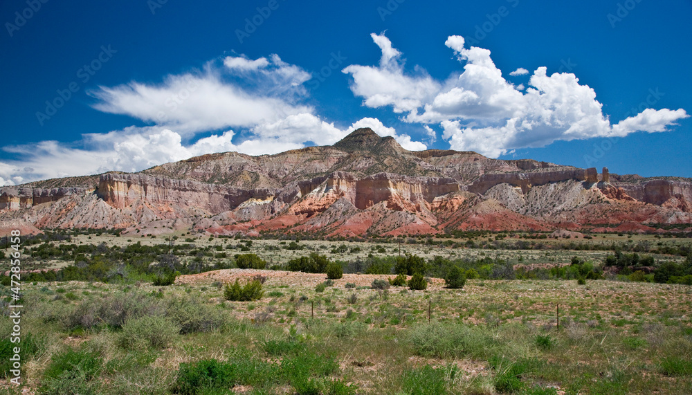 USA, New Mexico. White clouds in a blue sky over colorful sandstone cliffs.