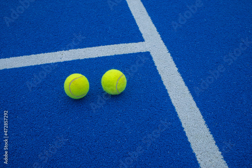 Two paddle tennis balls next to the lines of a paddle tennis court