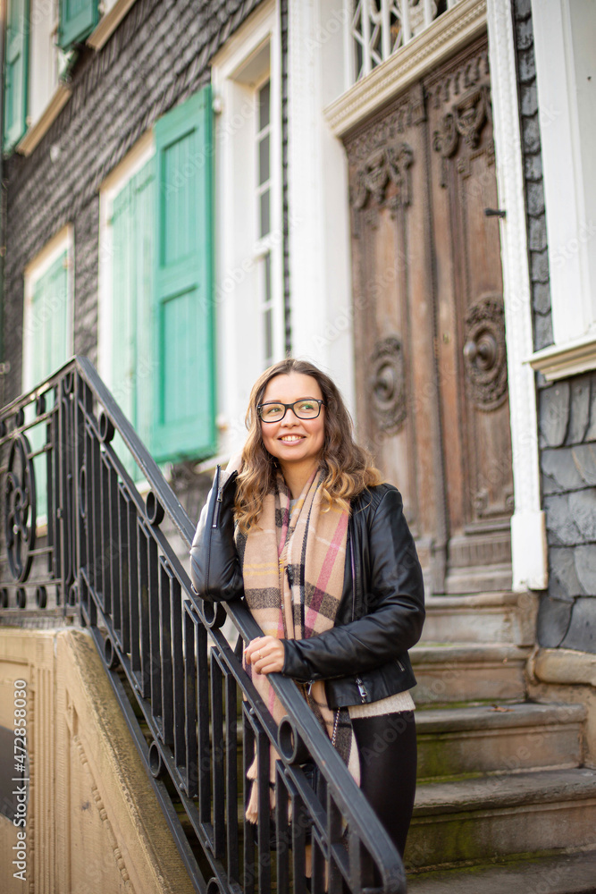 Smiling white young european woman with brown hair in glasses on stairs near old building