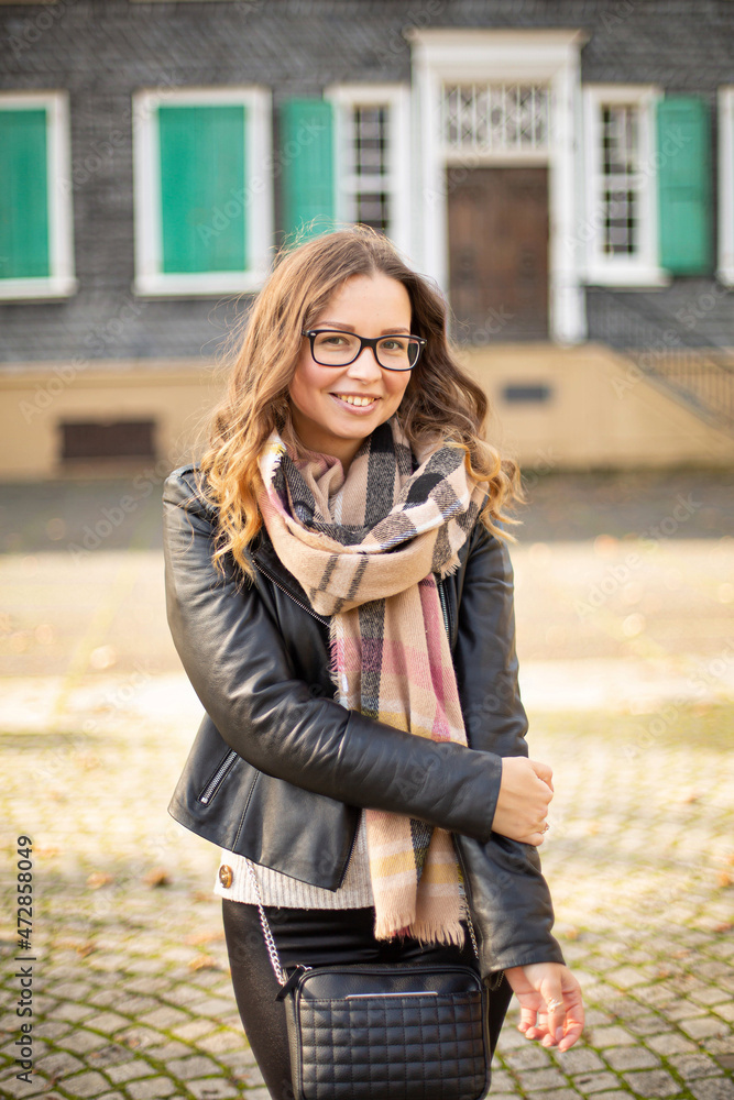 Pretty smiling white young european girl with brown hair in glasses with building behind in fall Pretty smiling white young european girl with brown hair in glasses with building behind in fall