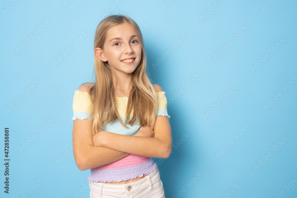 Smiling little blond girl posing with arms folded isolated over blue background. Smiling little blond girl posing with arms folded isolated over blue background.