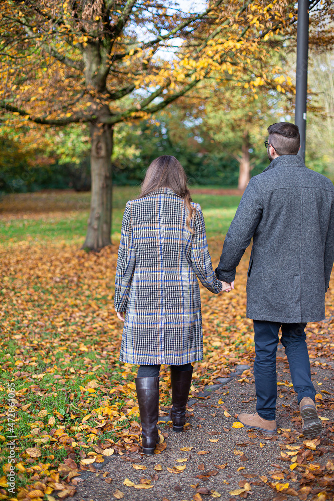 Obraz premium Turned back white young man and woman in autumn forest holding hands