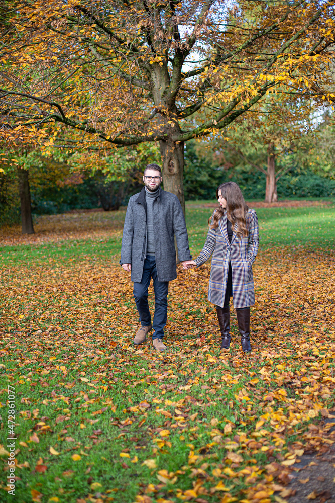 White young man and woman holding hands in autumn forest