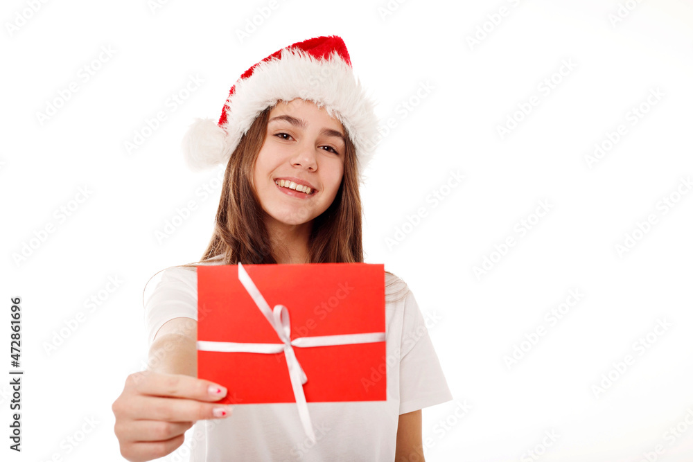 Happy young teenager girl in white t-shirt and santa claus red hat holds gift certificate isolated on white background. People lifestyle Christmas and New Year concept. Happy young teenager girl in white t-shirt and santa claus red hat holds gift certificate isolated on white background. People lifestyle Christmas and New Year concept.