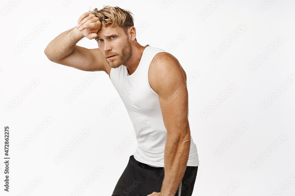 Image of tired sportsman wipe sweat on forehead and having break during jogging, workout in gym, standing over white background Image of tired sportsman wipe sweat on forehead and having break during jogging, workout in gym, standing over white background