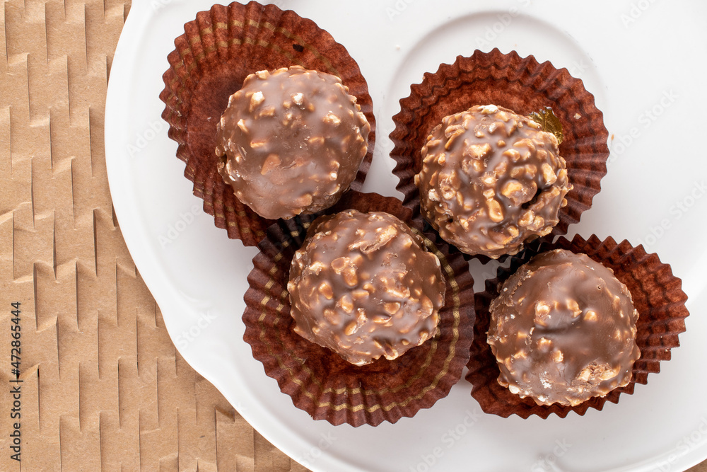 Several sweet chocolates with nuts with white dishes on craft paper, close-up, top view. Several sweet chocolates with nuts with white dishes on craft paper, close-up, top view.