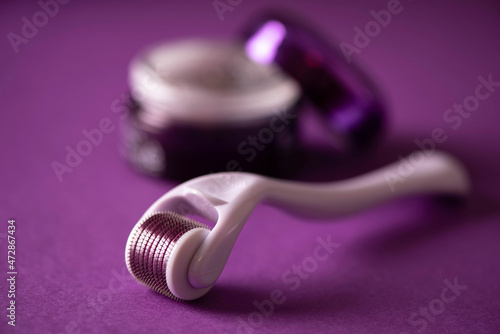 cosmetic face roller with cosmetic cream on purple background photo