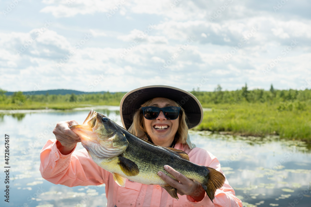 Woman fishing on a lake holding big bass catch. Lady holding largemouth bass  catch with sun shinning. Text space. Stock Photo