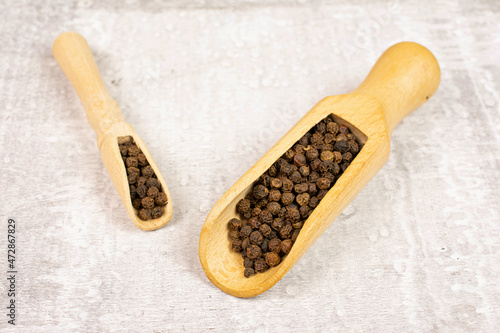 Lot of whole spicy black pepper in a wooden scoop on white background