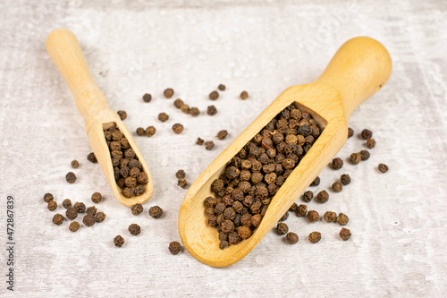 Lot of whole spicy black pepper in a wooden scoop on white background with some pepper scattered around