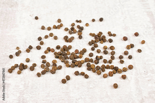 Lot of whole spicy black pepper on white background