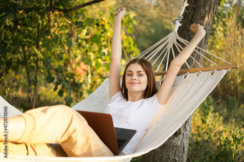 women outdoors lies in a hammock with a laptop freelance internet