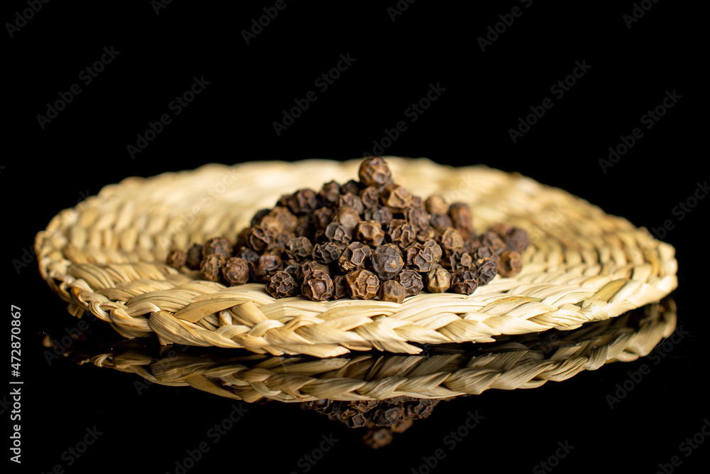 Lot of whole spicy black pepper isolated on black glass on bamboo coaster