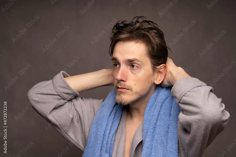 Young handsome tall slim white man with brown hair freshly out of shower with towel on shoulders in grey bathrobe on grey background Young handsome tall slim white man with brown hair freshly out of shower with towel on shoulders in grey bathrobe on grey background
