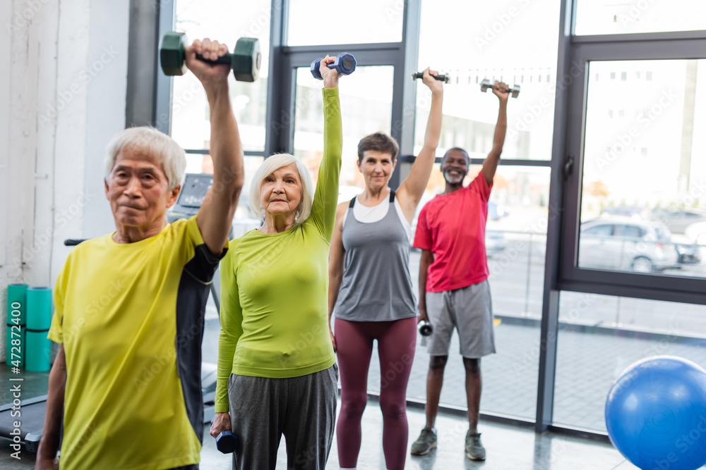 Obraz premium Group of interracial senior people exercising with dumbbells in sports center.